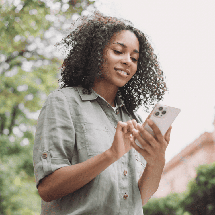 Young woman buying insurance on their mobile phone online while taking a leisurely walk in the park.