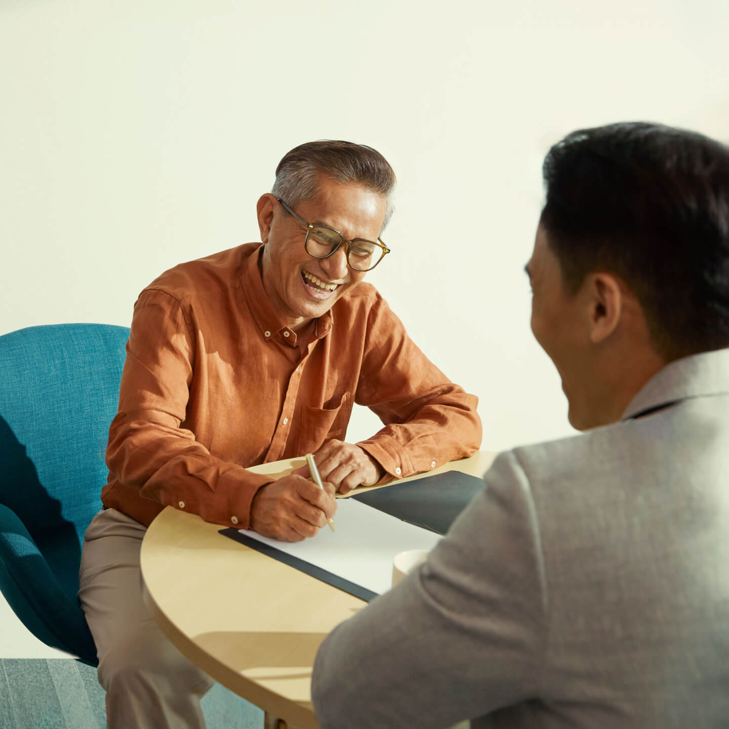 Two businessmen sitting at a table reviewing a physical document.
