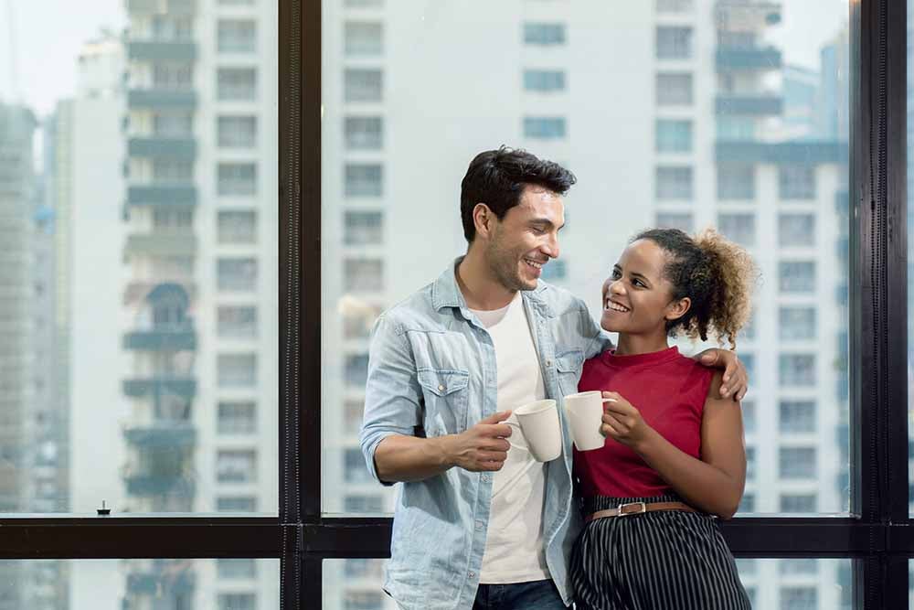 Un jeune couple debout devant une fenêtre de copropriété