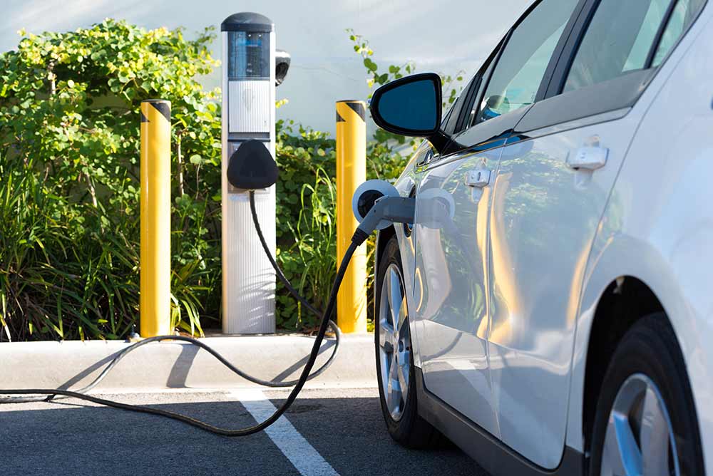 Véhicule électrique en recharge à l'extérieur avec un arbuste en arrière-plan