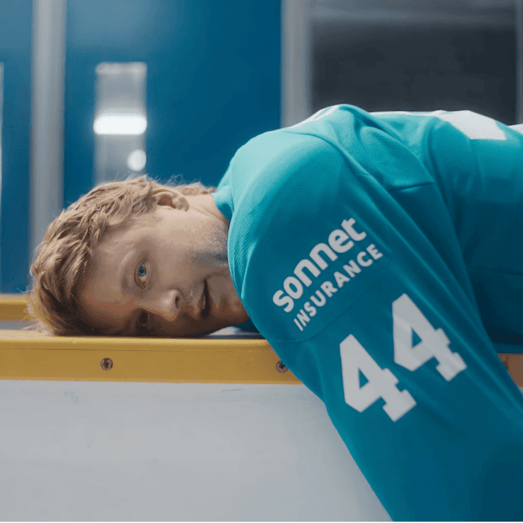 Morgan Rielly of the Toronto Maple Leafs wearing a teal Sonnet Insurance jersey with number 44, lying on the boards inside a hockey arena.