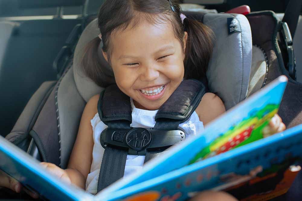Little girl reading a book in a car seat