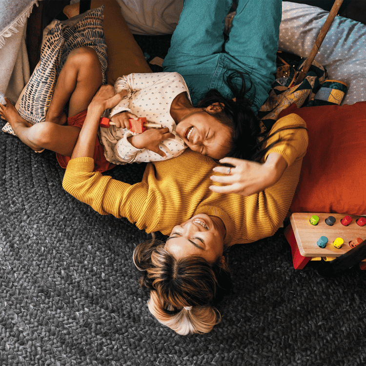Une mère et son enfant allongés sur un tapis, riant et jouant ensemble à la maison.