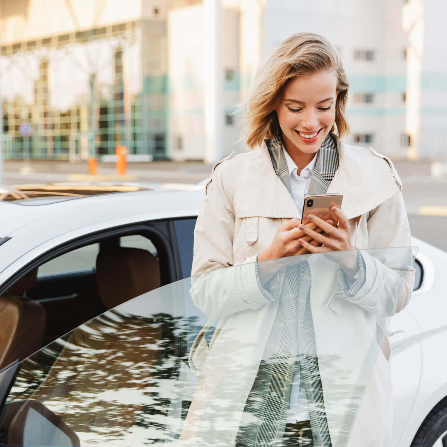 Une femme sourit en regardant son téléphone cellulaire, debout, près de sa voiture, sur une rue de Toronto.