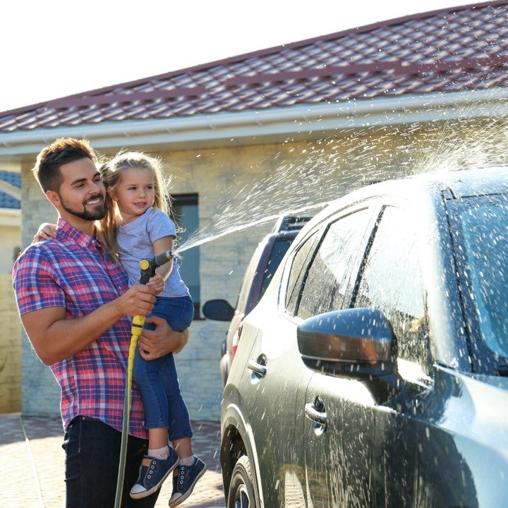 Father washing car with daughter outside their home