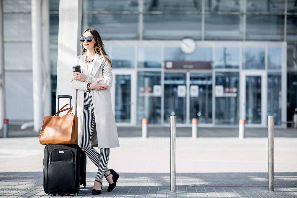 Une femme transporte ses bagages à l’extérieur d’un aéroport