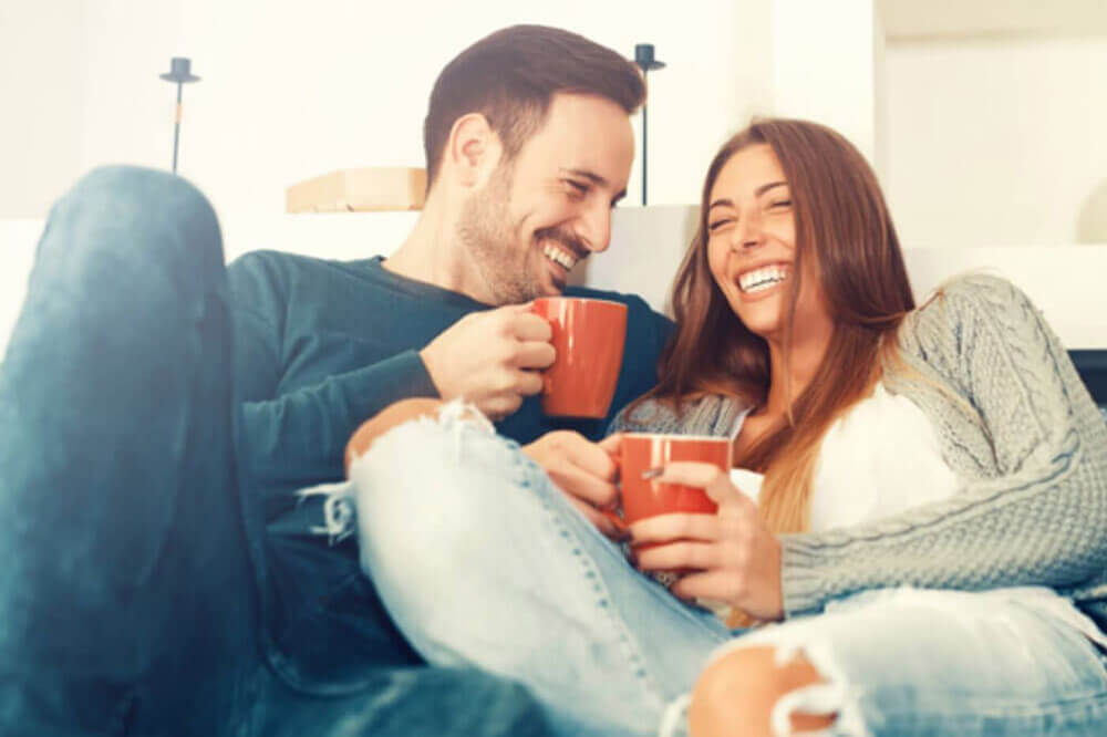Couple laughing and drinking tea on the couch