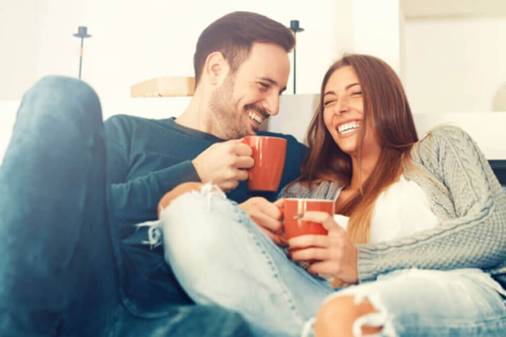 Un couple qui rit et boit du thé sur le canapé