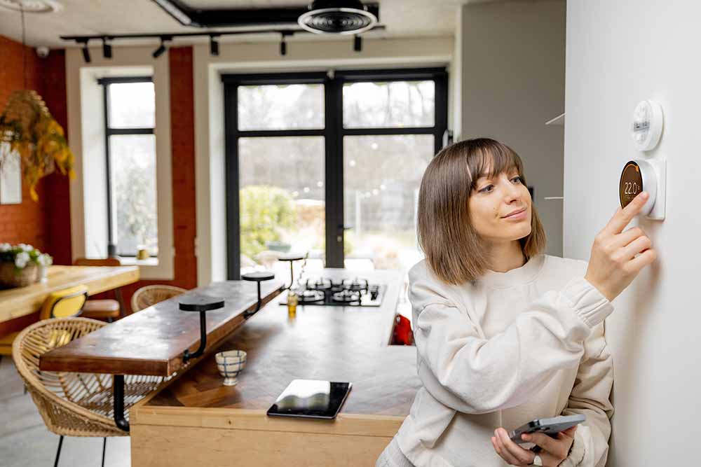 Une femme ajuste son thermostat à la maison