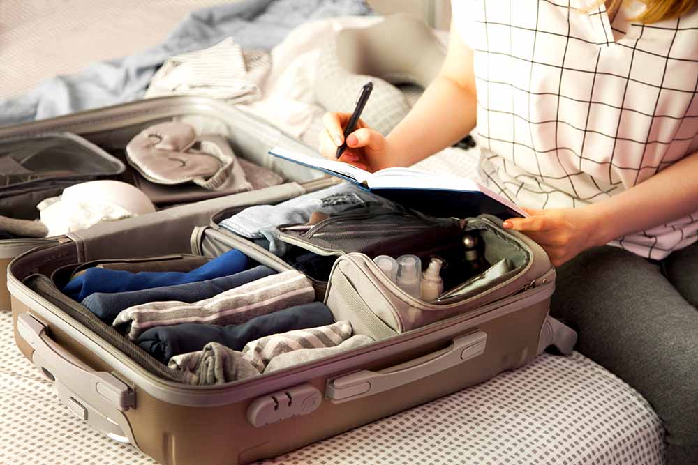 Femme dressant une liste d’articles à emporter avec une valise ouverte