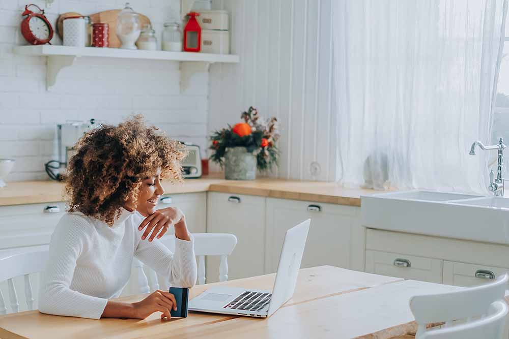Une femme assise devant un ordinateur portable, tenant une carte bancaire