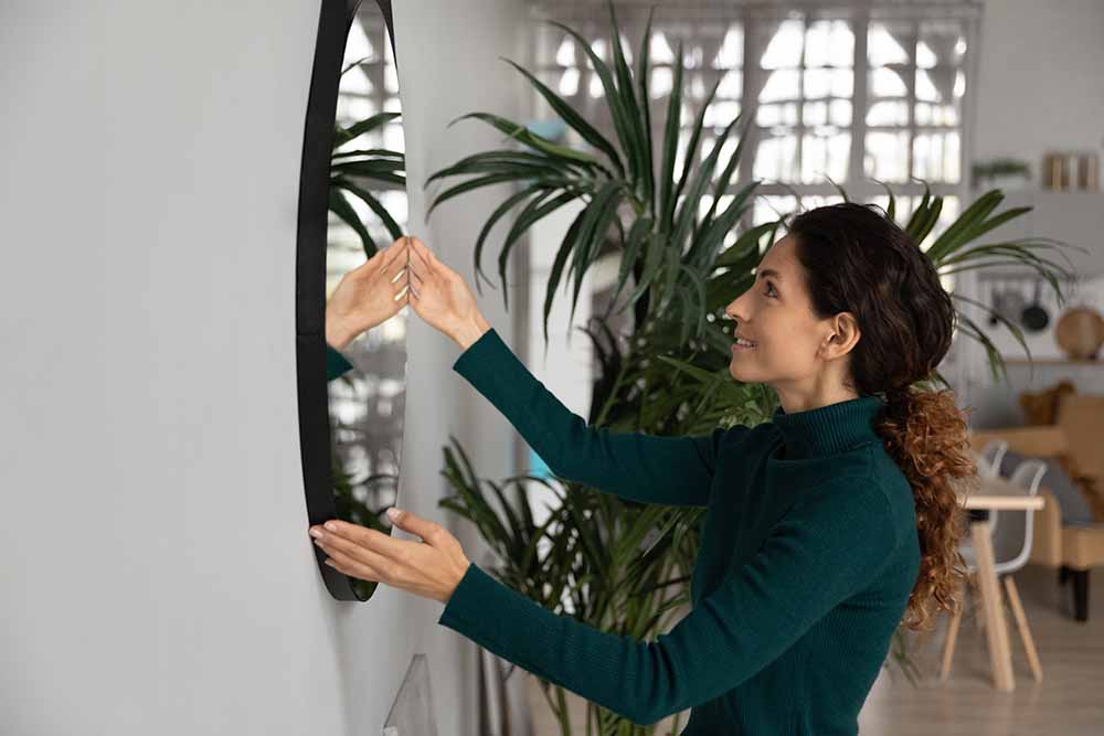 Une femme accrochant un miroir dans un appartement