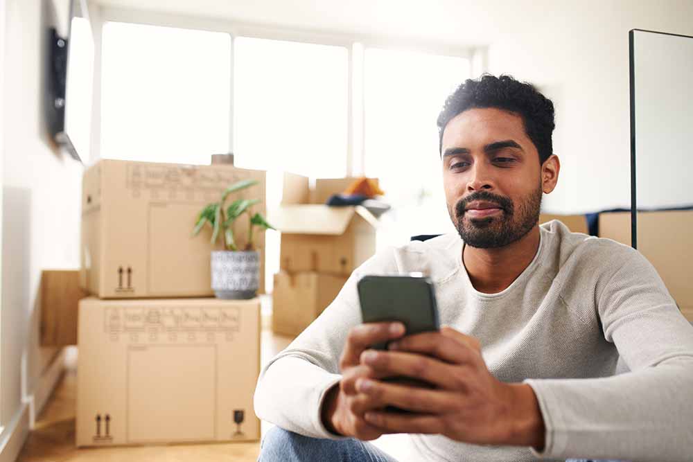 Un homme assis au milieu des boîtes sur son téléphone intelligent