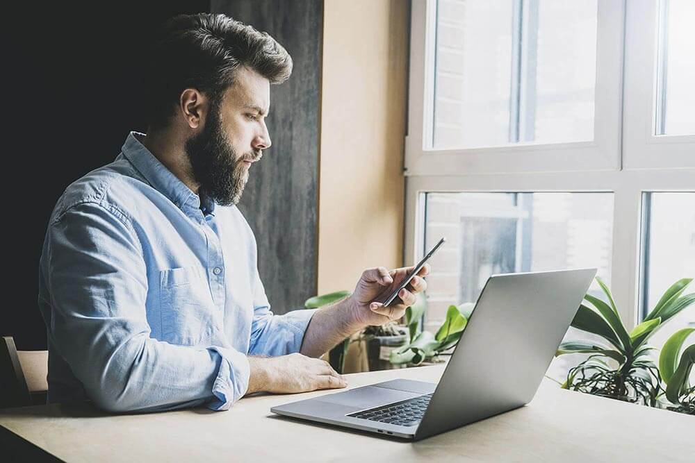 Man checking his cellphone with his laptop open