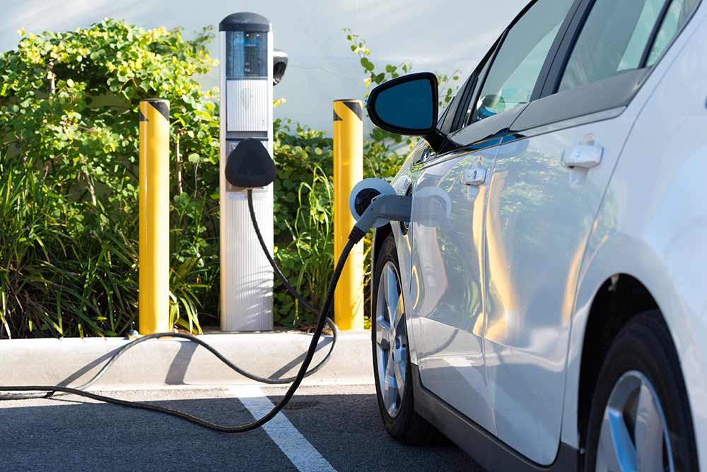 Electric vehicle charging outside with green bush in the background