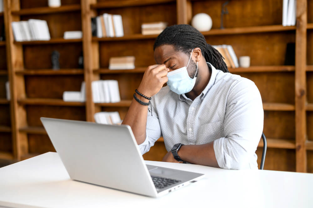 Tired African-American man wearing mask feeling exhausted, worrying about his job