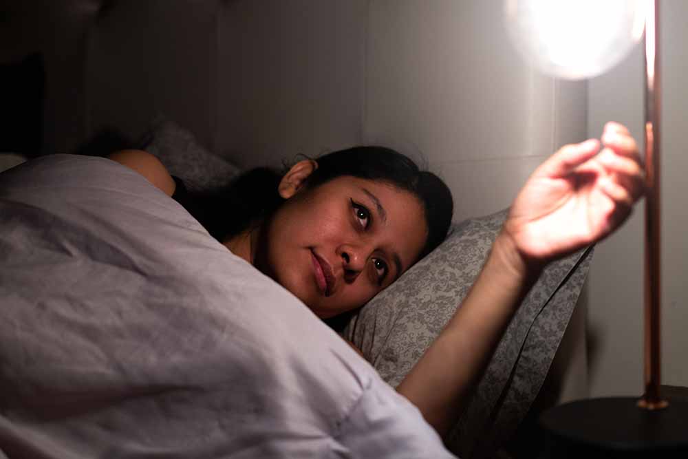 Une femme éteint une lampe, couchée sur un lit